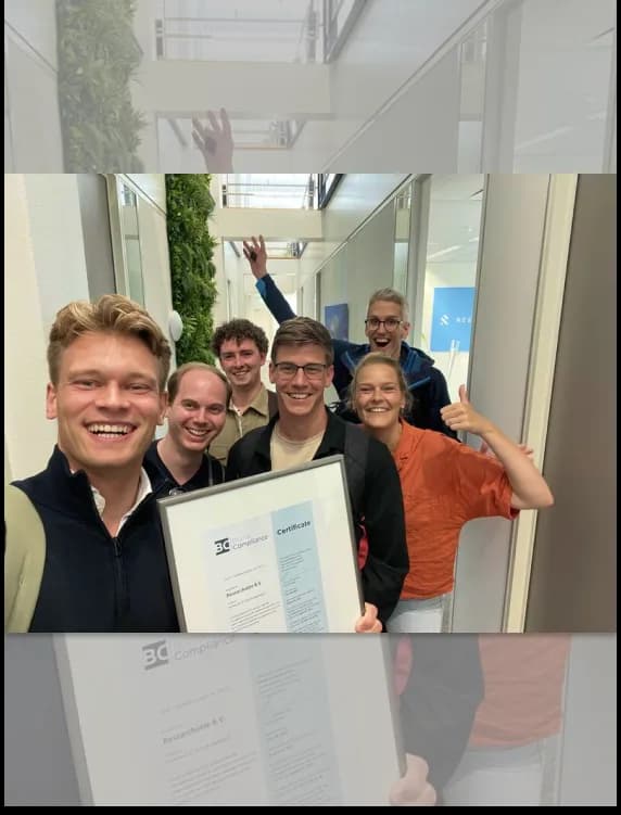 Smiling Researchable team in the office corridor celebrating the ISO 27001 certification with the framed certificate